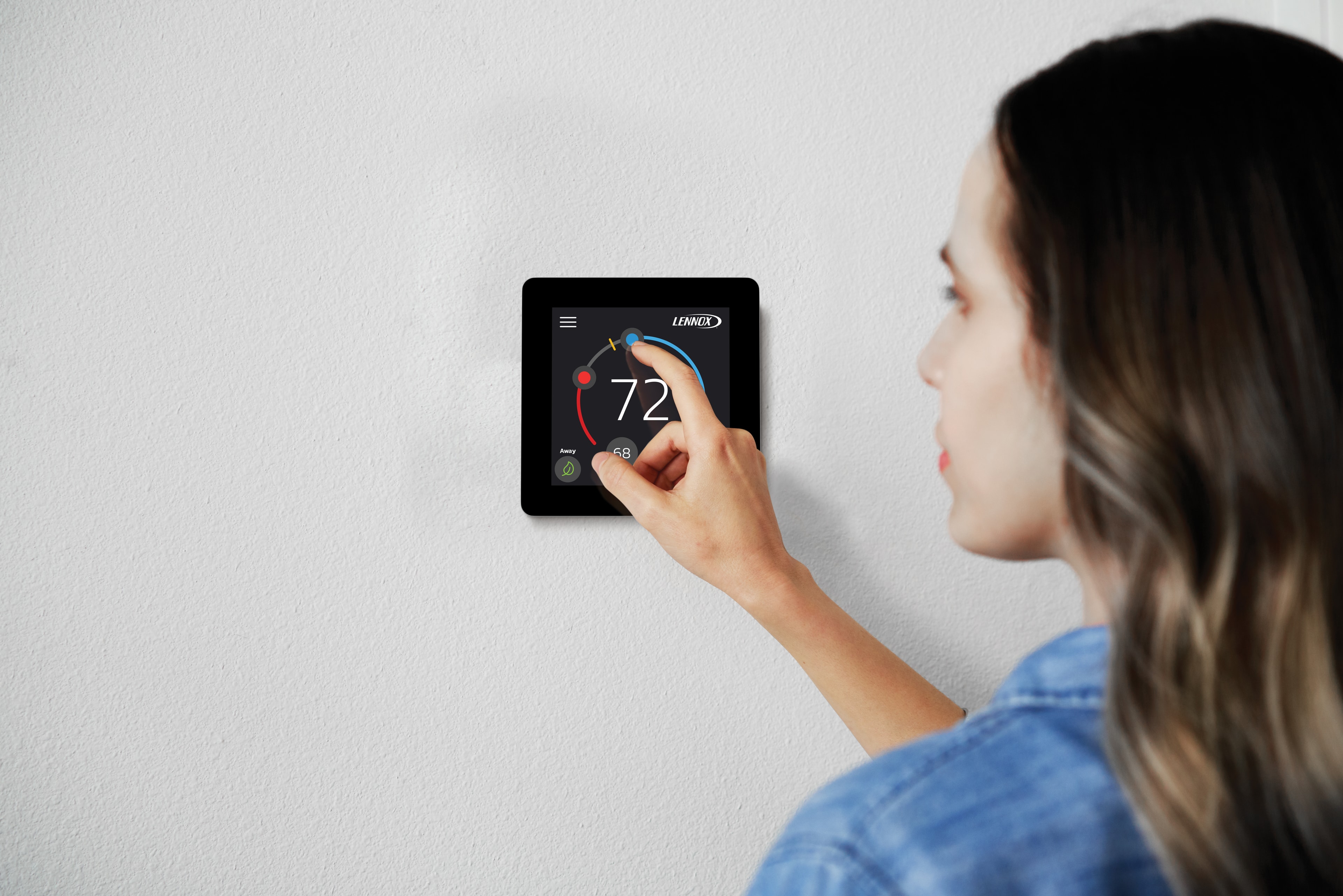 Homeowner adjusting Lennox iComfort smart thermostat on wall